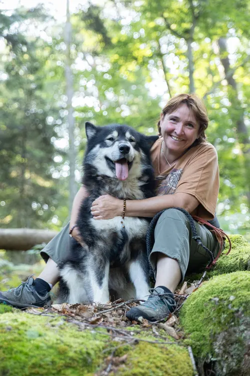Laetitia souriante, assise avec son chien en forêt