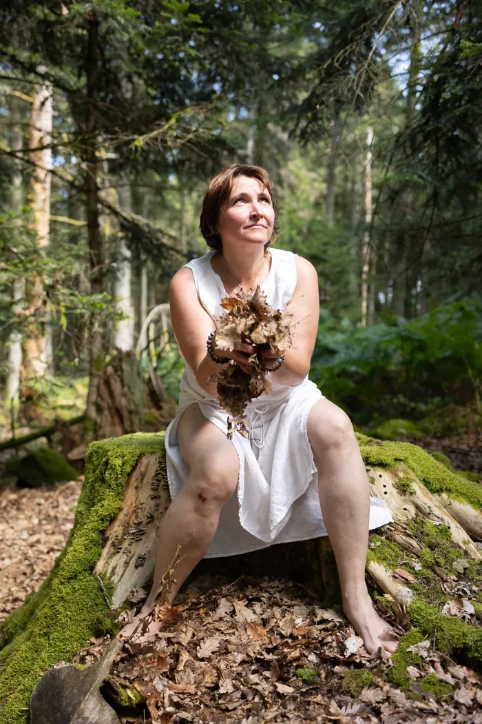 Laetitia Fischer, naturopathe à Grendelbruch, assise en forêt, des feuilles dans les mains
